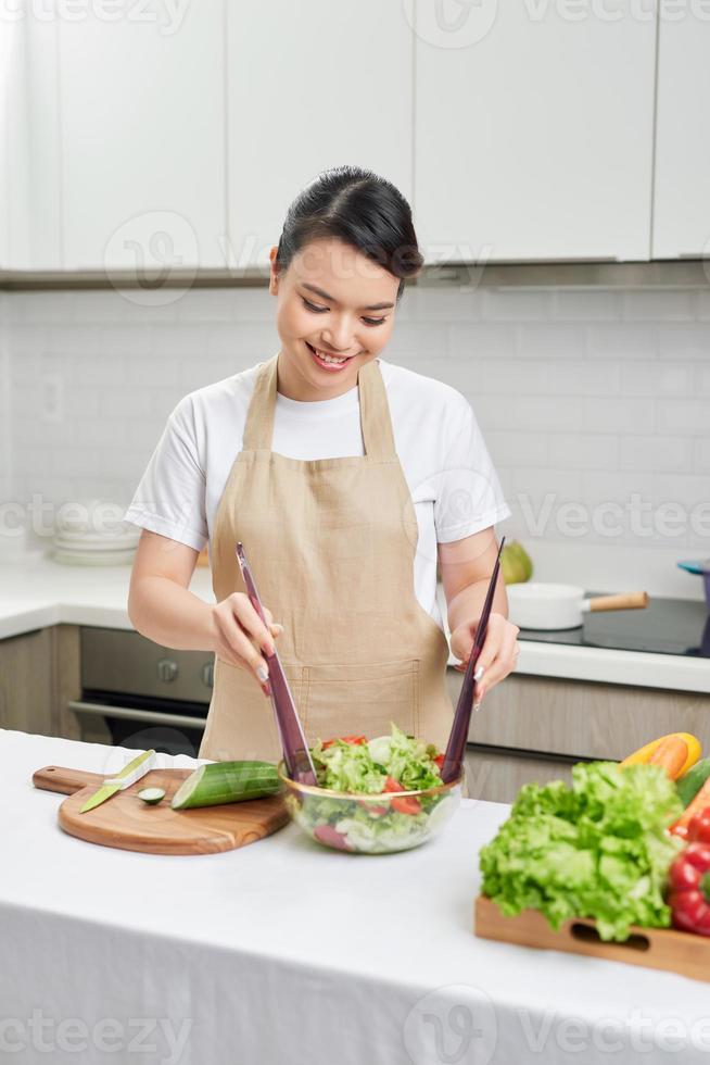 Happy young housewife mixing vegetable salad photo