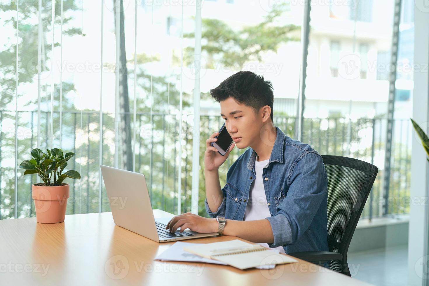 man talking on mobile phone, working from home. Portrait of pensive asian businessman using laptop computer, planning project, communication in modern office photo