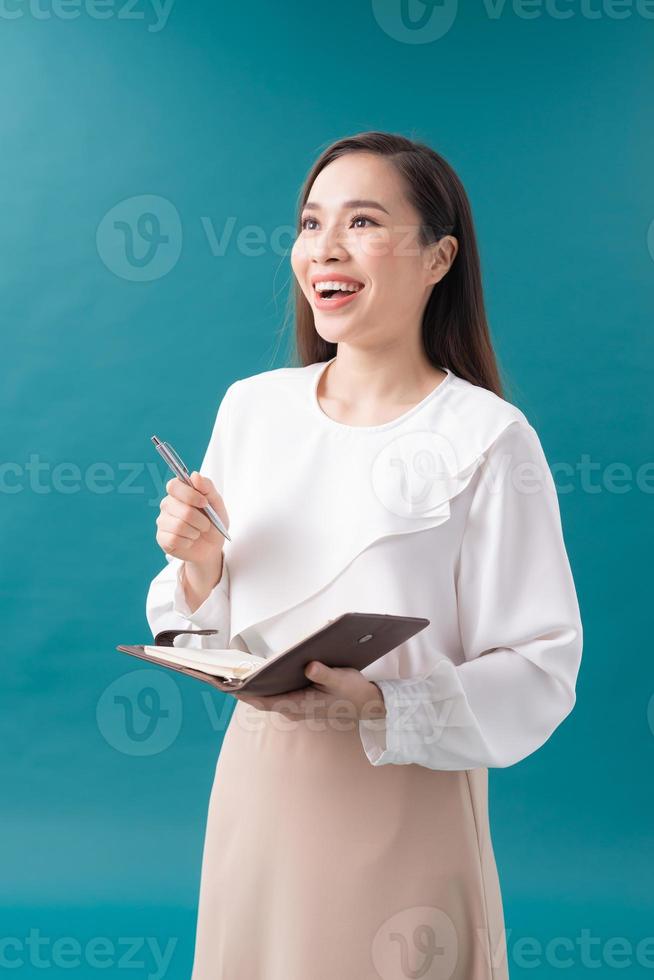 Lovely young entrepreneur woman making notes in a notebook smiling against a blue background photo