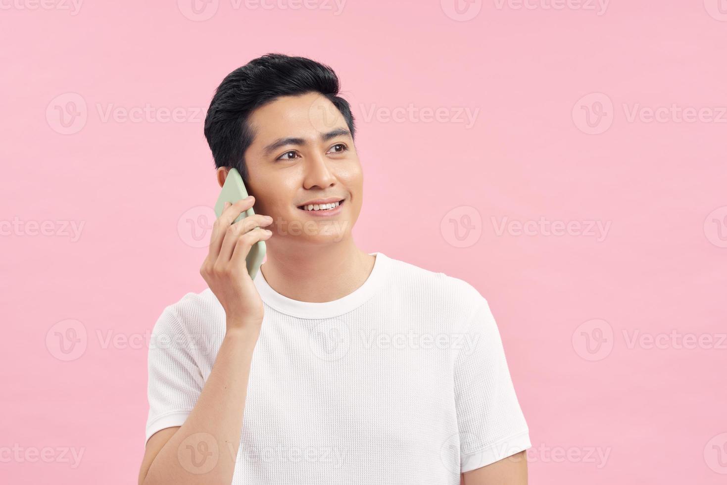 A portrait of an Asian young man talking on a phone isolated on pink background photo