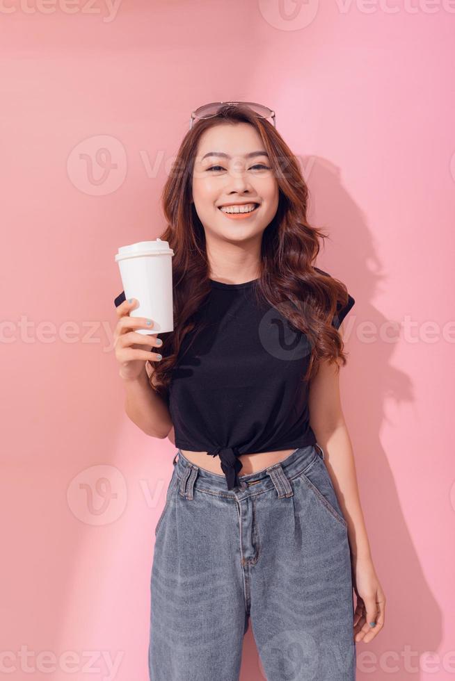 Photo of pensive woman holding takeout coffee stands over pink wall