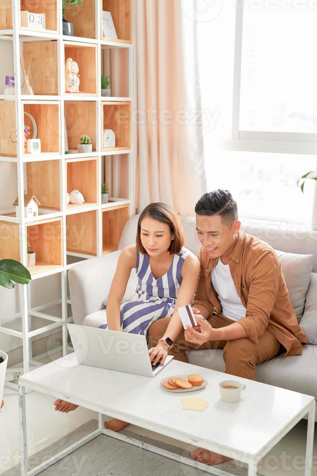 pareja feliz en casa pagando facturas con laptop y tarjeta de crédito foto