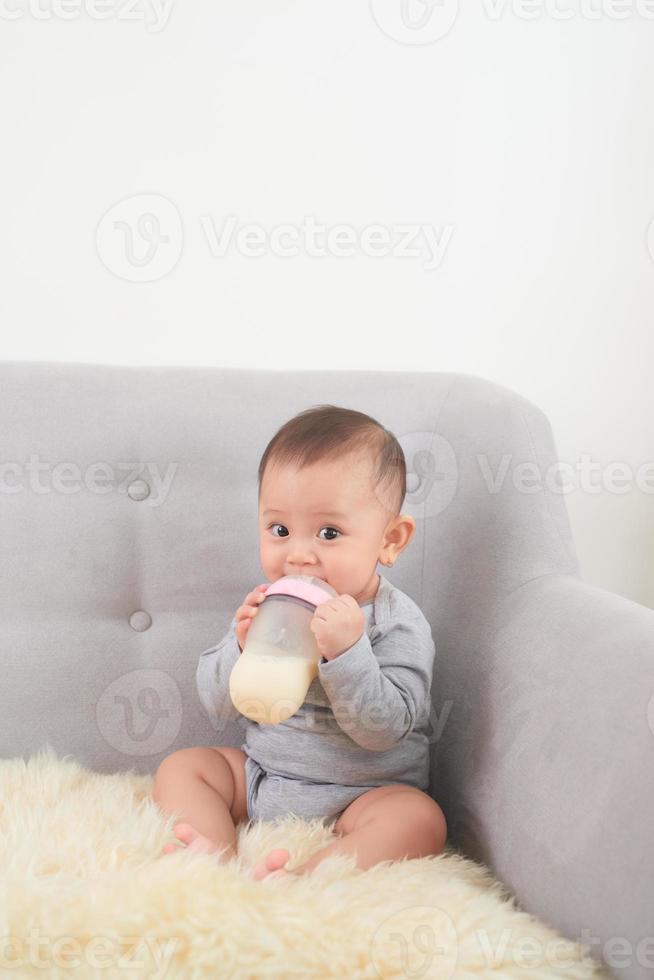 una niña pequeña y linda bebe leche mientras está acostada en un sofá azul en casa foto