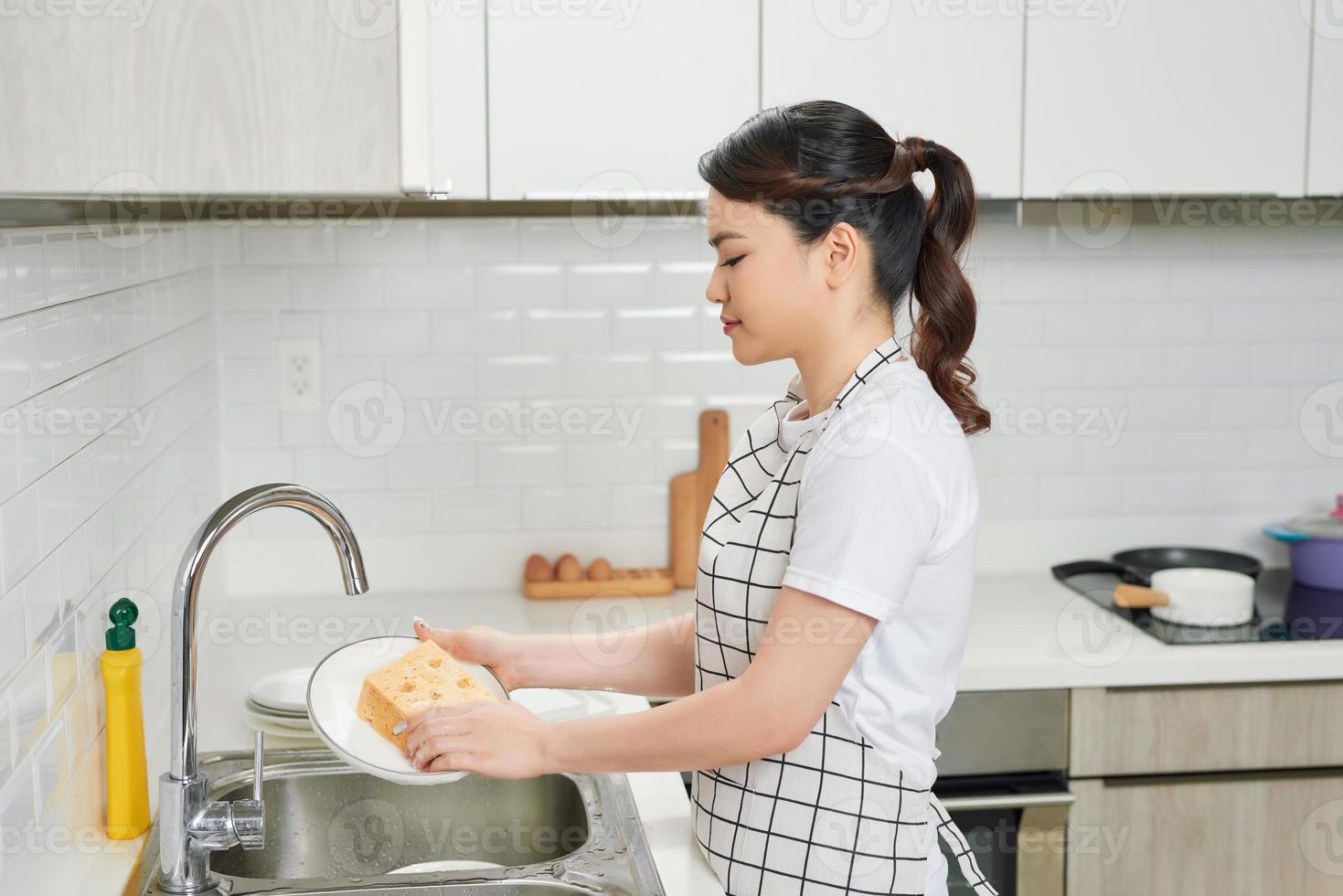 Kitchen porter cleaning white plates in sink in professional kitchen photo