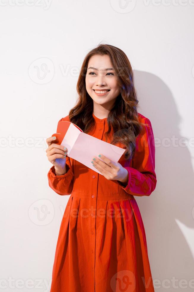 Sorprendida mujer joven asiática sosteniendo una tarjeta de felicitación mientras estaba aislada en rosa foto