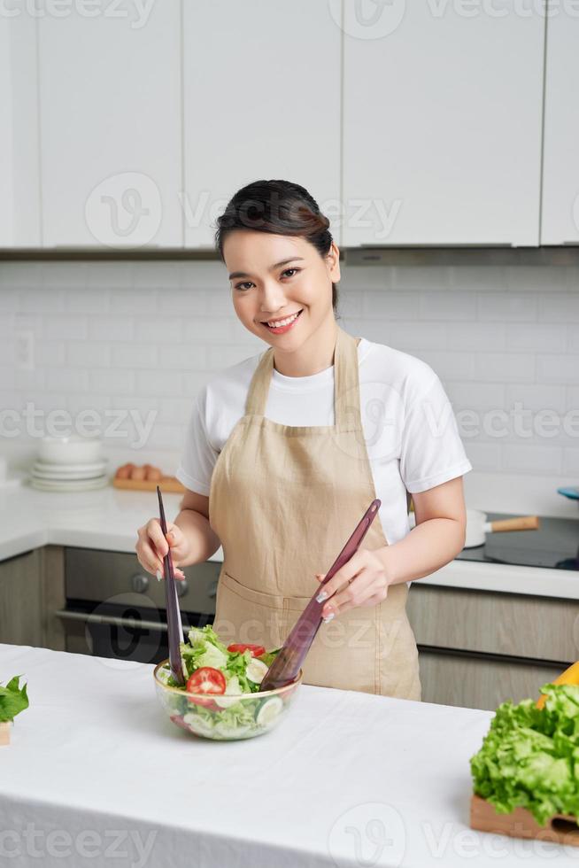 Beautiful young woman is preparing vegetable salad in the kitchen photo