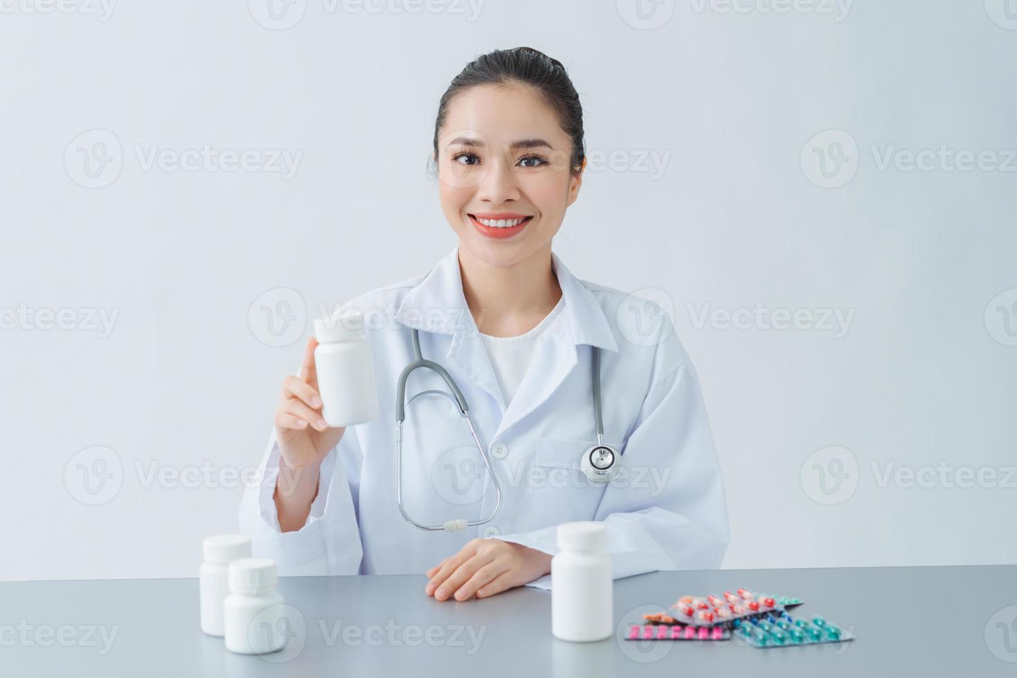 Female doctor sitting at desk, holding bottle with white pills photo