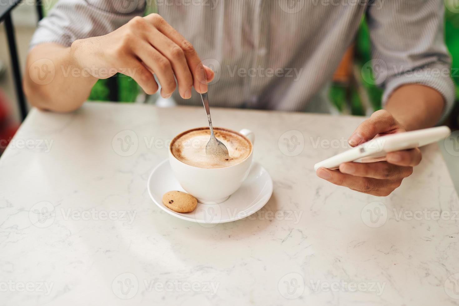 A man drinks cappuccino with a smartphone in his hand in a cozy restaurant photo