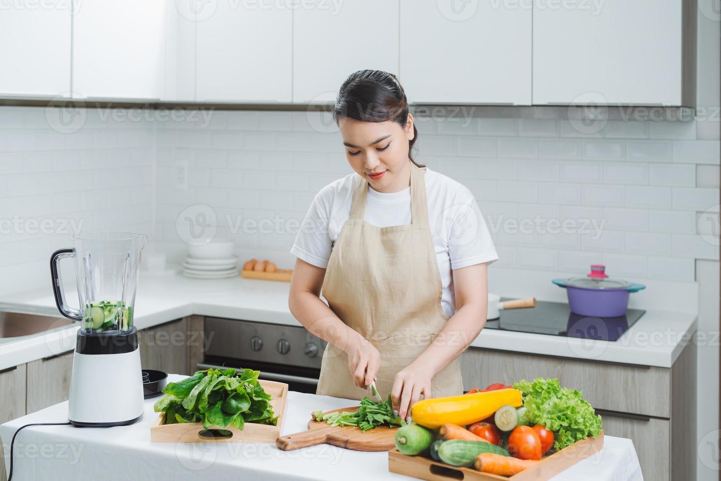 close up of young woman with blender and green vegetables making detox shake or smoothie at home photo