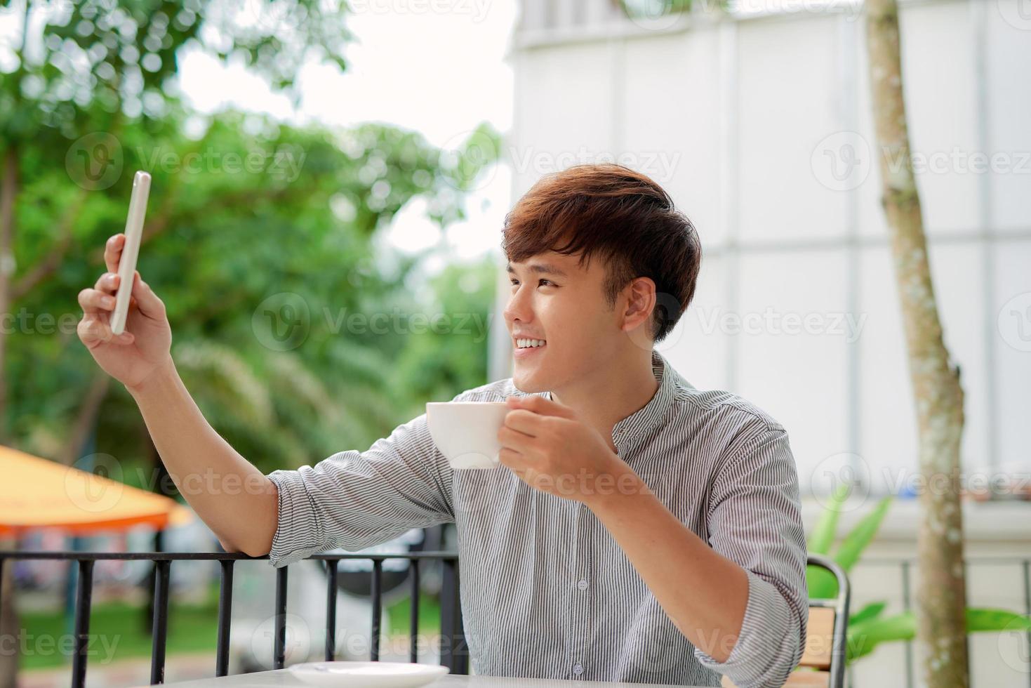 young man spending time in outdoor restaurant having a coffee and taking selfie photo