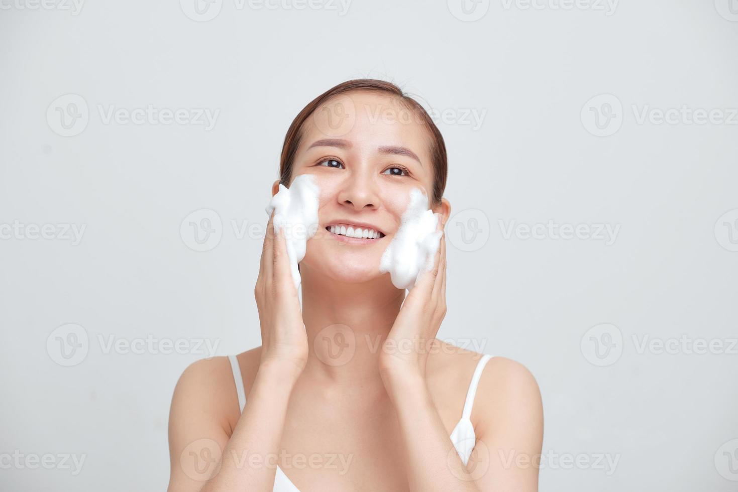 Happy attractive young Asian woman applying foaming cleanser on her face over white background. photo