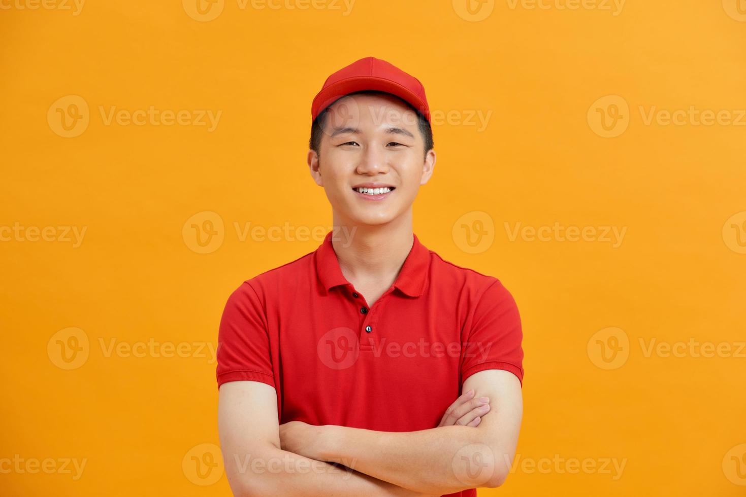 Smiling delivery man in red uniform standing with arm crossed - isolated on white background photo