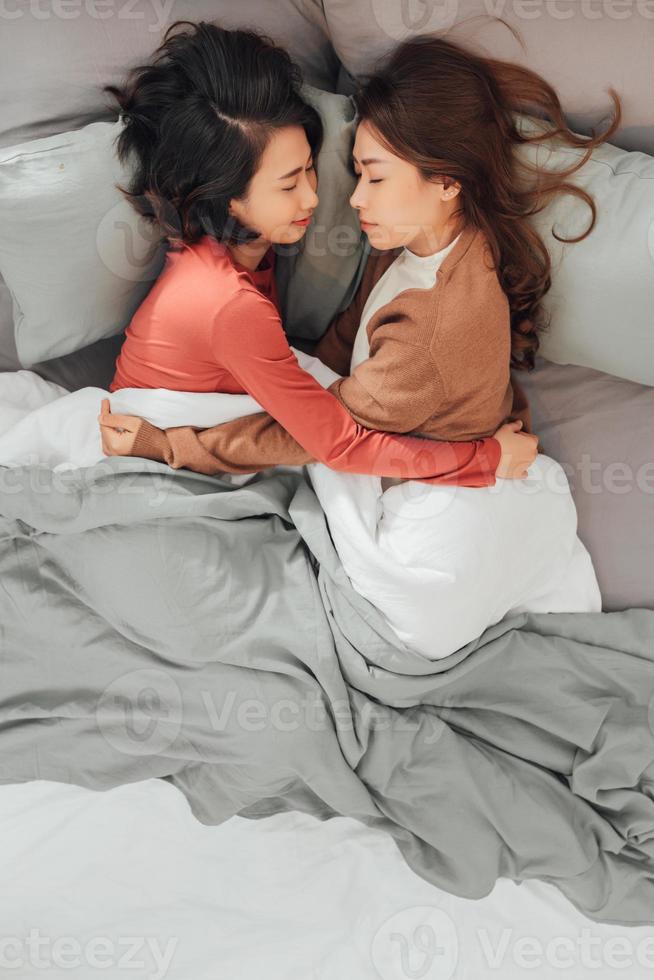 Young lesbian women in love embracing while lying don on bed at home. photo