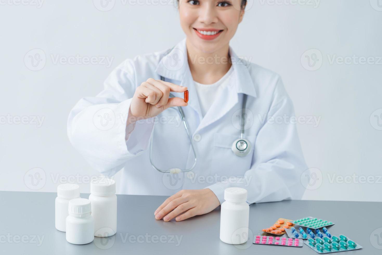 Beautiful female physician medicine doctor holding jar of pills in hands and writing prescription on special form photo