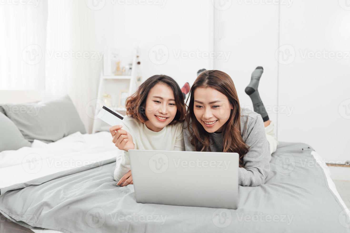 Two happy women shopping online with credit card and laptop at home photo