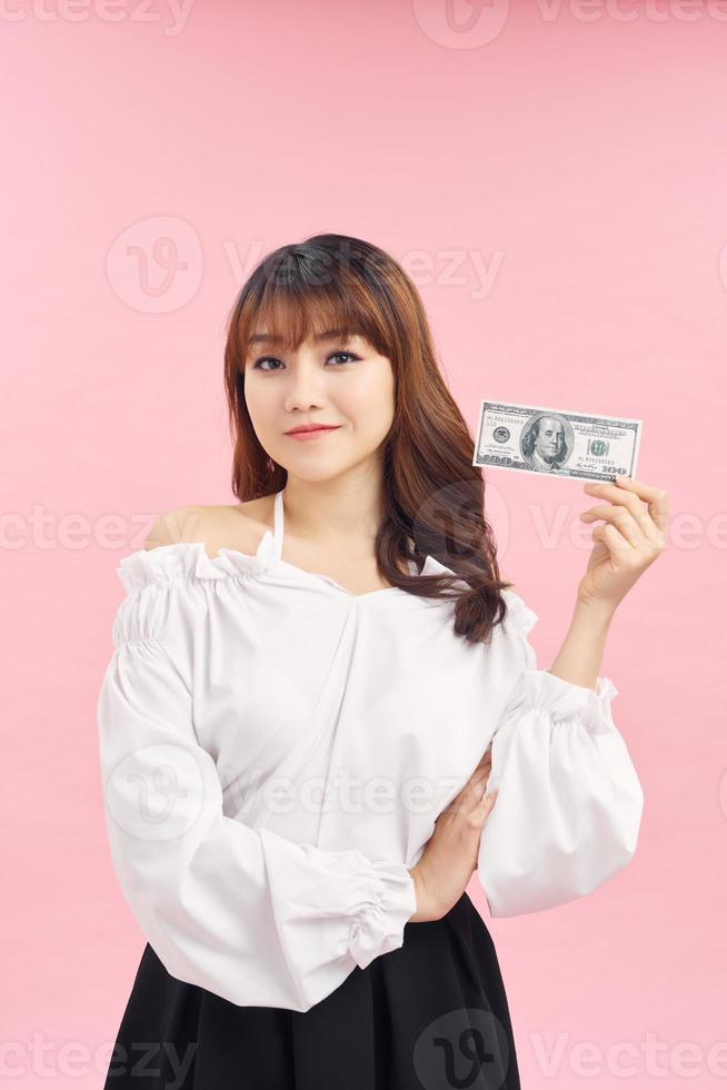 Portrait of happy joyous female 30s demonstrating lots of money dollar currency while using her mobile phone isolated over pink background photo