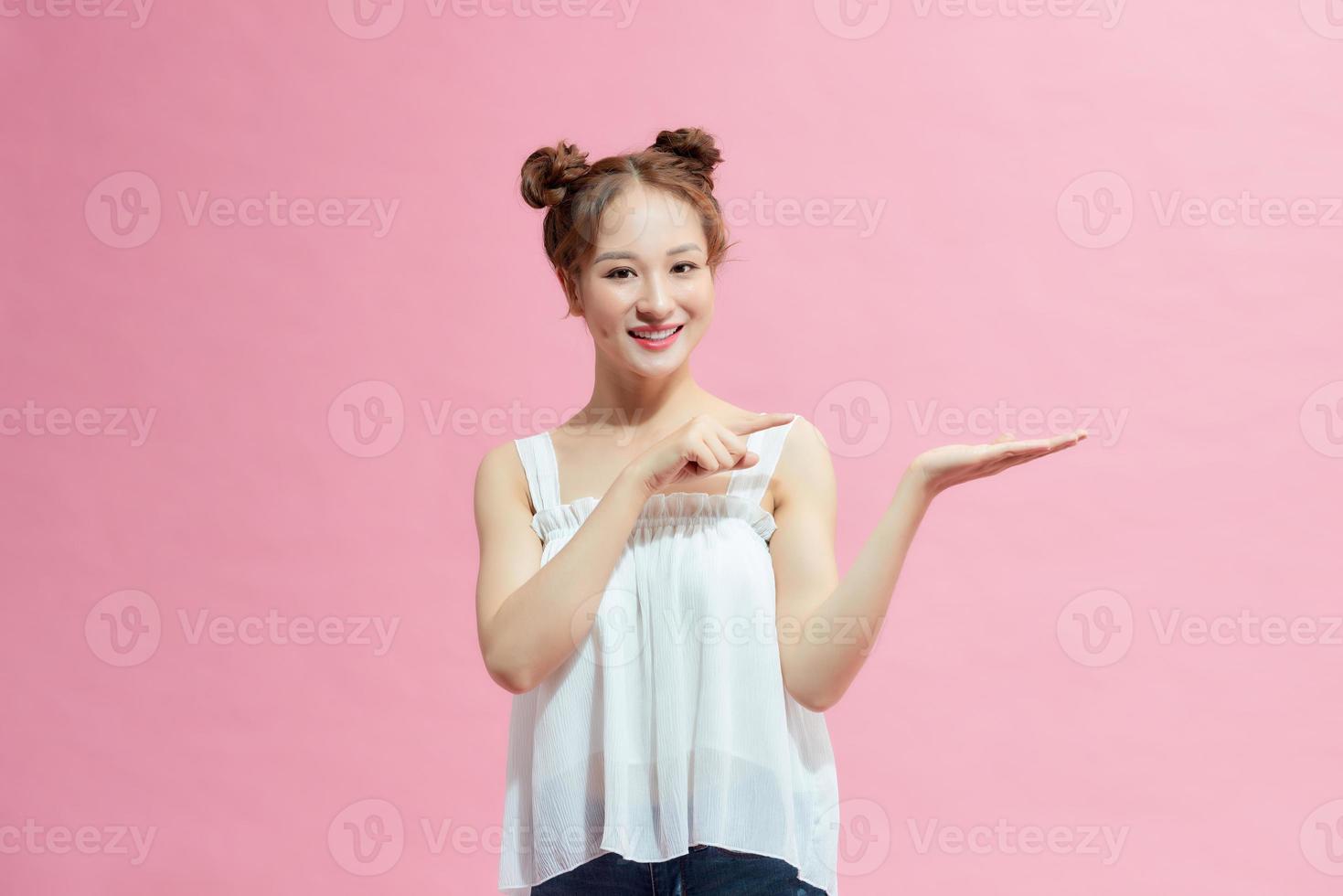 happy woman smiling and pointing finger at copy space at palm of hand isolated over pink photo