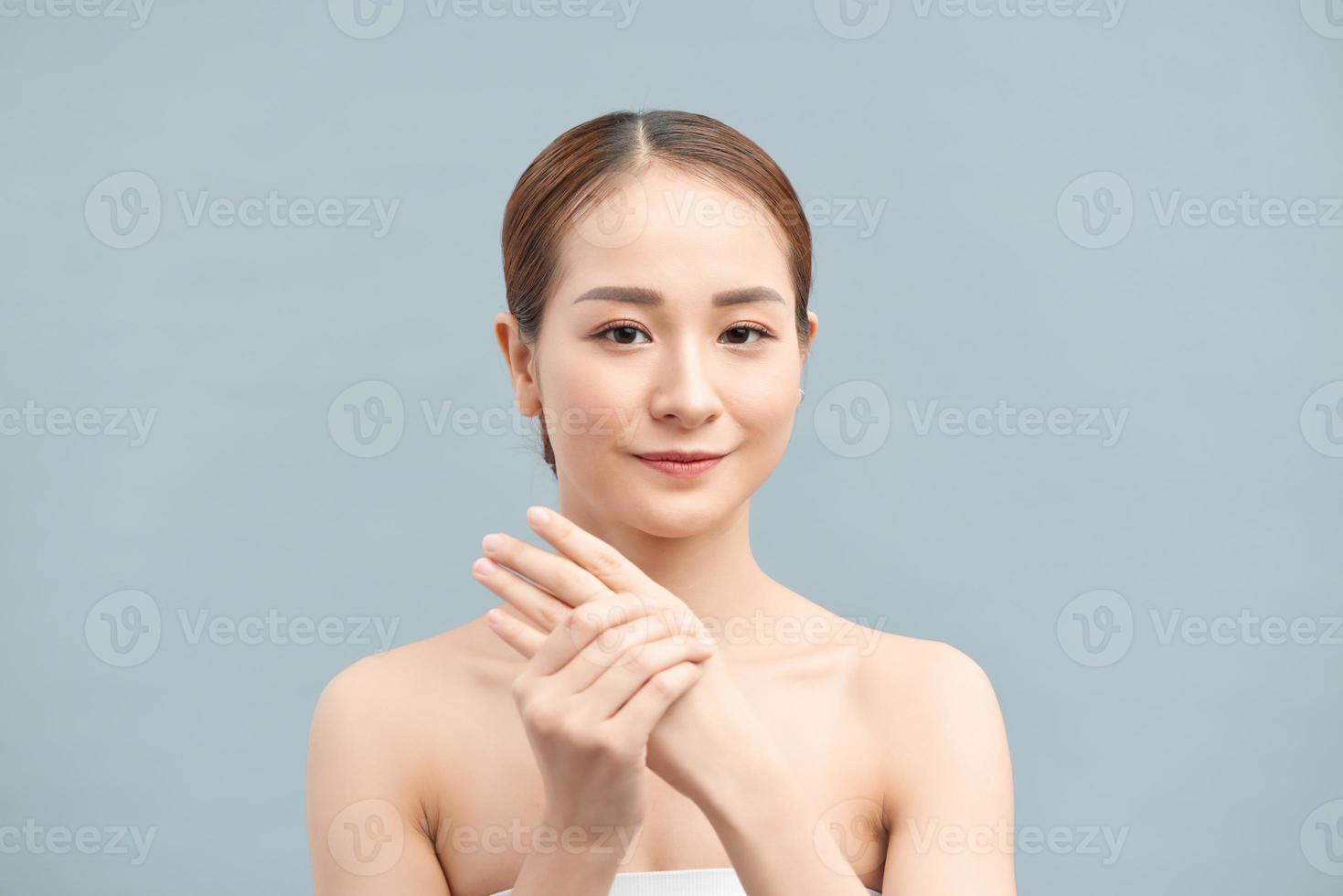 Portrait of happy smiling beautiful young woman touching skin or applying cream, isolated over violet background photo