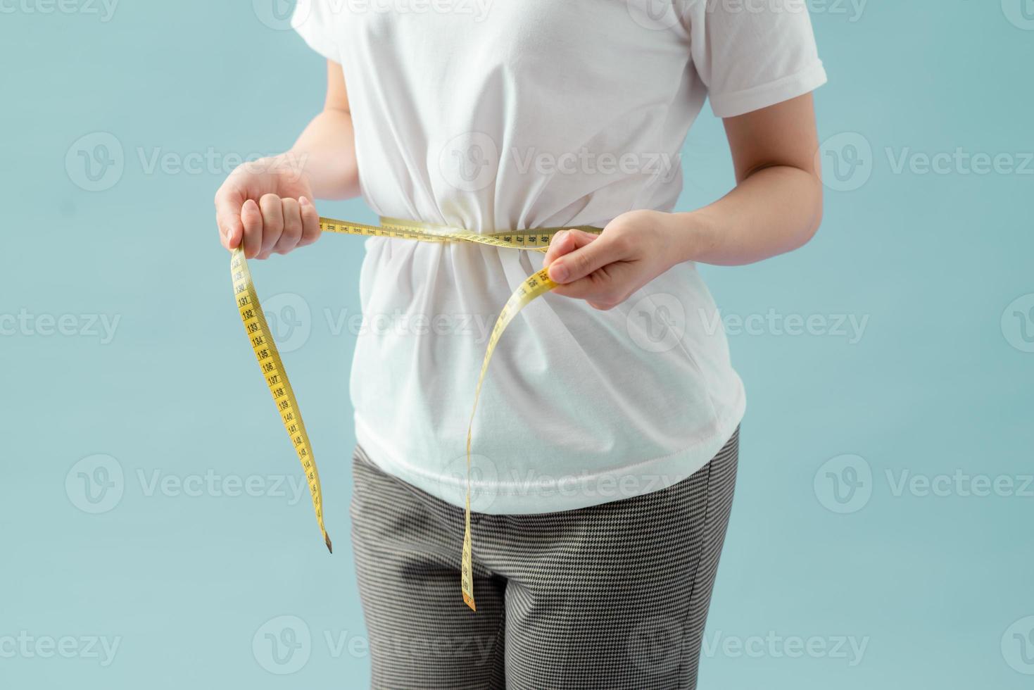 Weight loss, slim body, healthy lifestyle concept. Fit fitness girl measuring her waistline with measure tape on blue photo