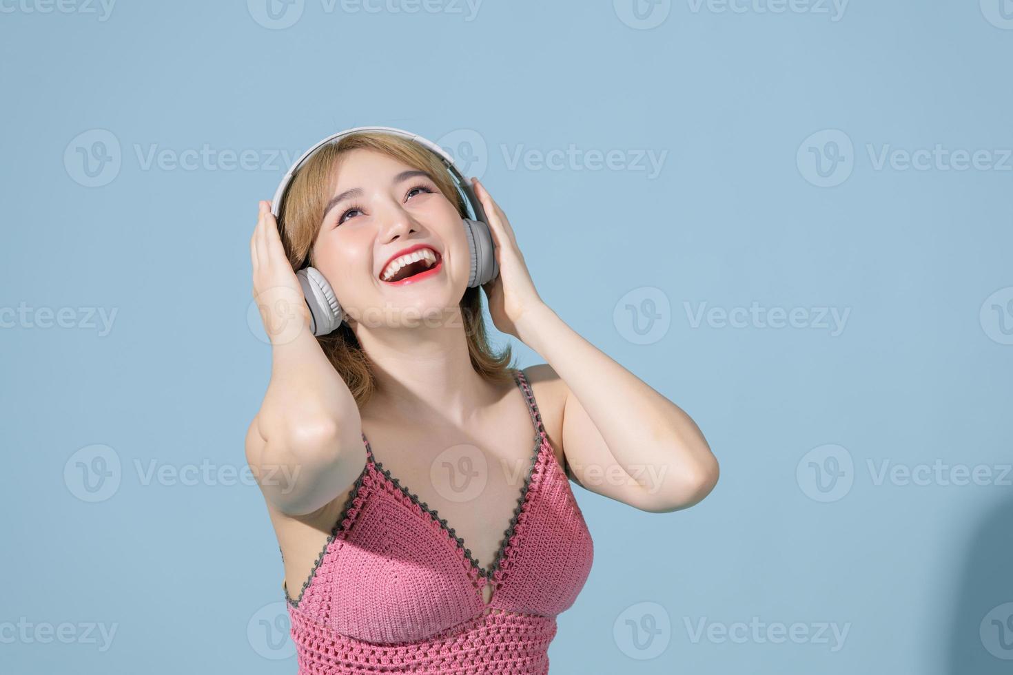 Studio shot of happy Asian millennial girl smiles gladfully looks away uses smartphone and headphone photo