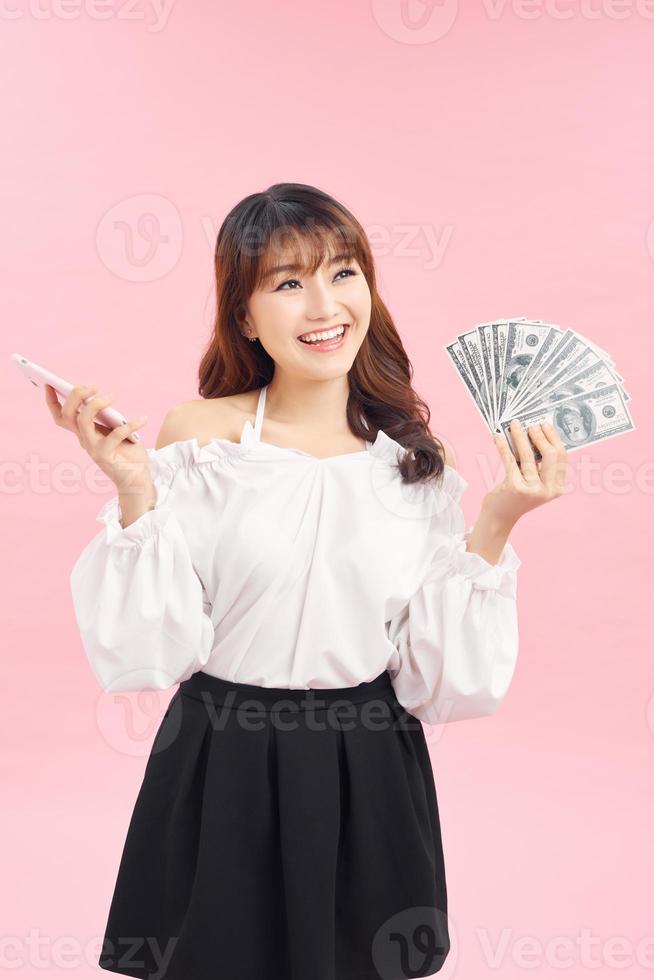 Portrait of young asian woman showing bunch of money banknotes on pink background photo
