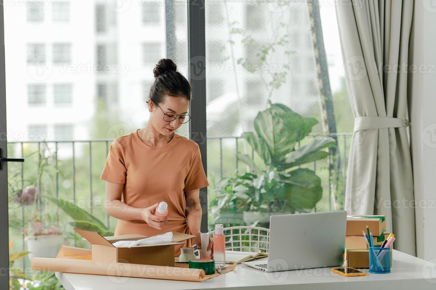 mujer joven que ejecuta una tienda de cosméticos en línea empacando productos para su envío foto