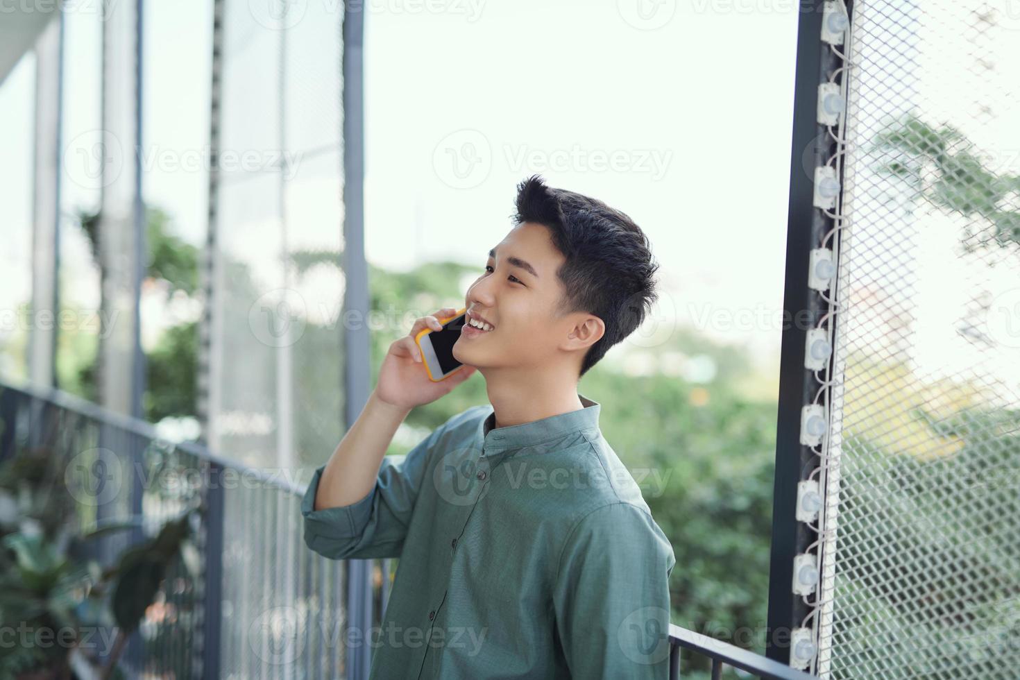 Young handsome man having conversation on smartphone at balcony at sunny summer day photo