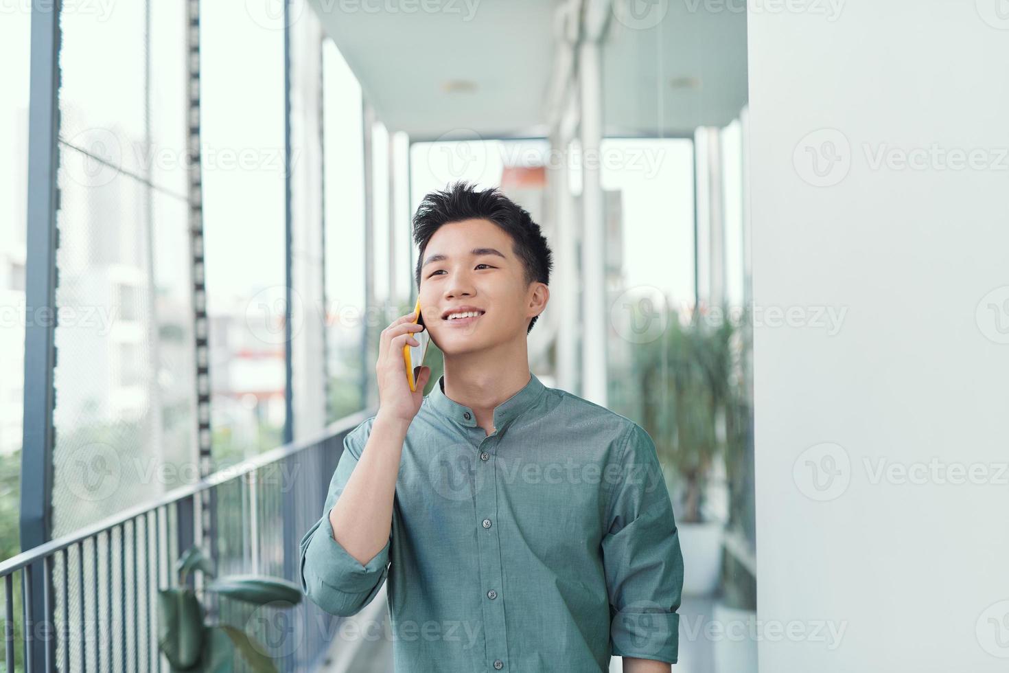 Happy man speaking on cellphone standing on balcony in city in summer day photo
