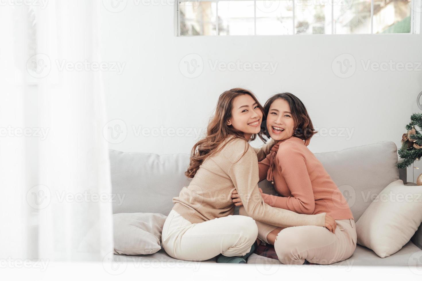 Two happy friends or sisters hugging sitting on a couch in the living room at home photo