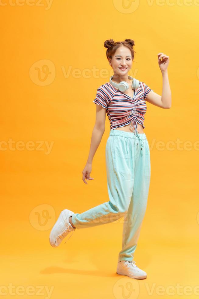 Full length portrait of a cheerful casual asian woman jumping isolated over yellow background photo