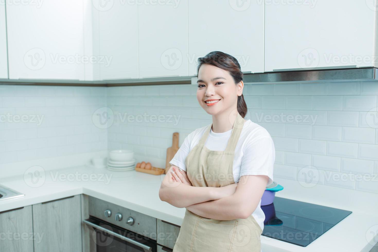 Portrait of young woman standing with arms crossed against kitchen background photo