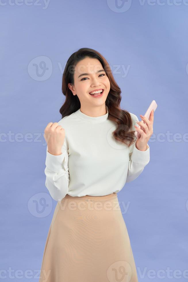 Portrait of a cheerful girl looking at mobile phone isolated over purple background photo