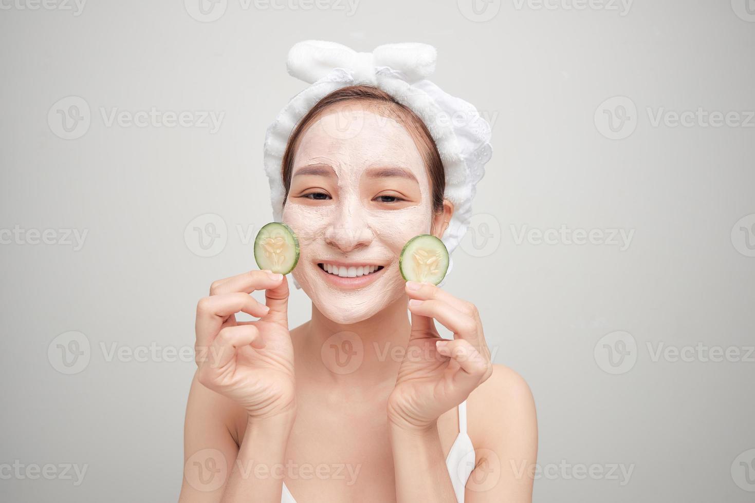 Young woman with clay facial mask holding cucumber slices isolated on white background photo
