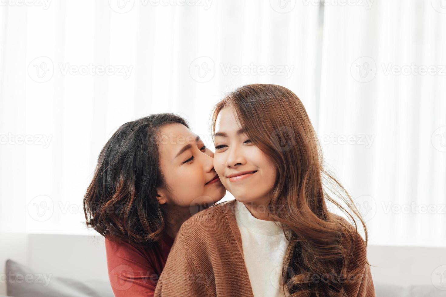 Affectionate girl kissing her happy sister or friend in the living room at home with a homey background photo