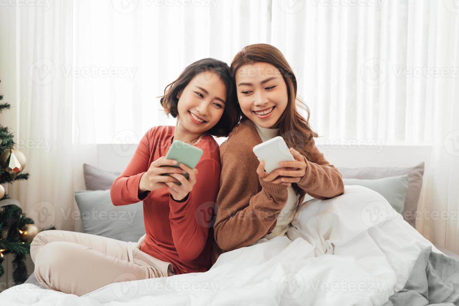 joven feliz lesbiana lgbtq pareja o amigos sosteniendo un teléfono inteligente usando un teléfono móvil en casa foto