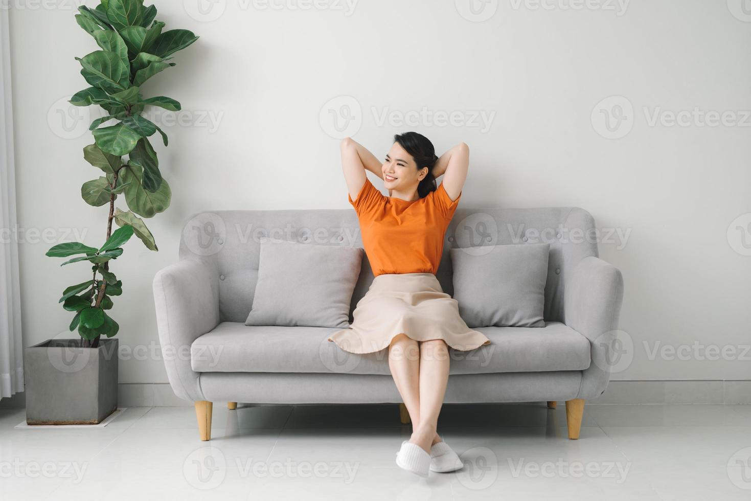 Peaceful young woman with hands behind head relaxing on cozy sofa at home photo