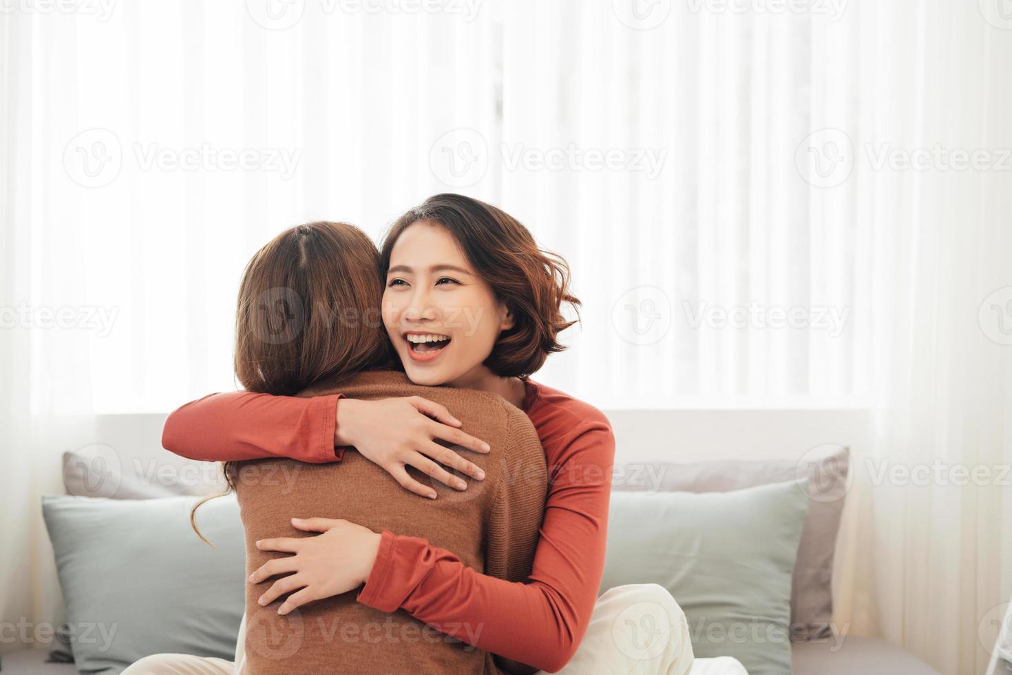 Two happy friends or sisters hugging sitting on a couch in the living room at home photo