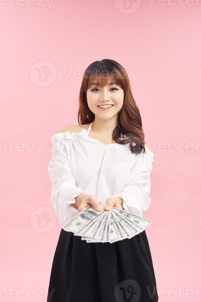 Portrait of a cheerful young woman holding money banknotes and celebrating isolated over pink background photo