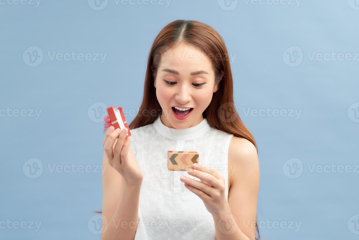 Cheerful young woman holding small gift box isolated on a blue background photo