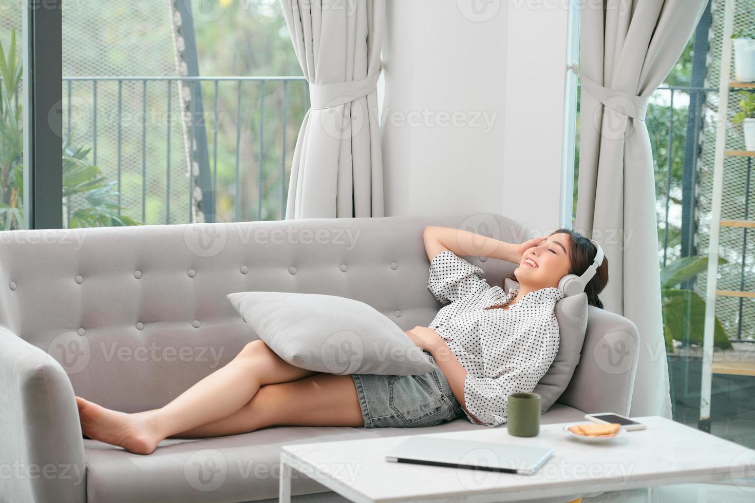 feliz joven mujer relajada con auriculares sentados en el sofá y escuchando música de meditación en el tiempo libre foto