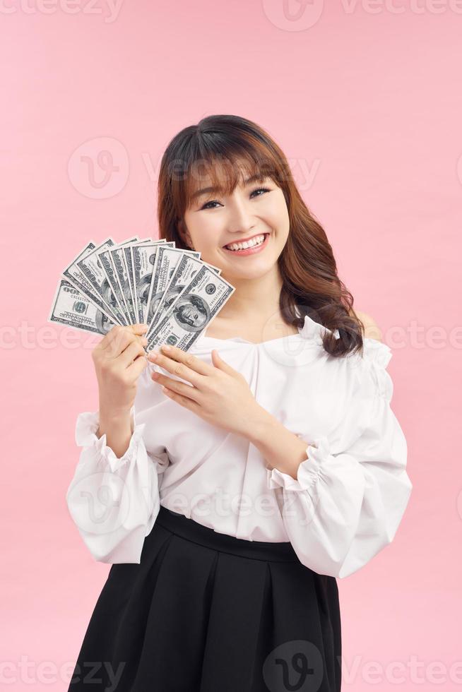 imagen de una joven asiática sonriente parada aislada sobre un fondo rosado. mirando cámara con dinero. foto