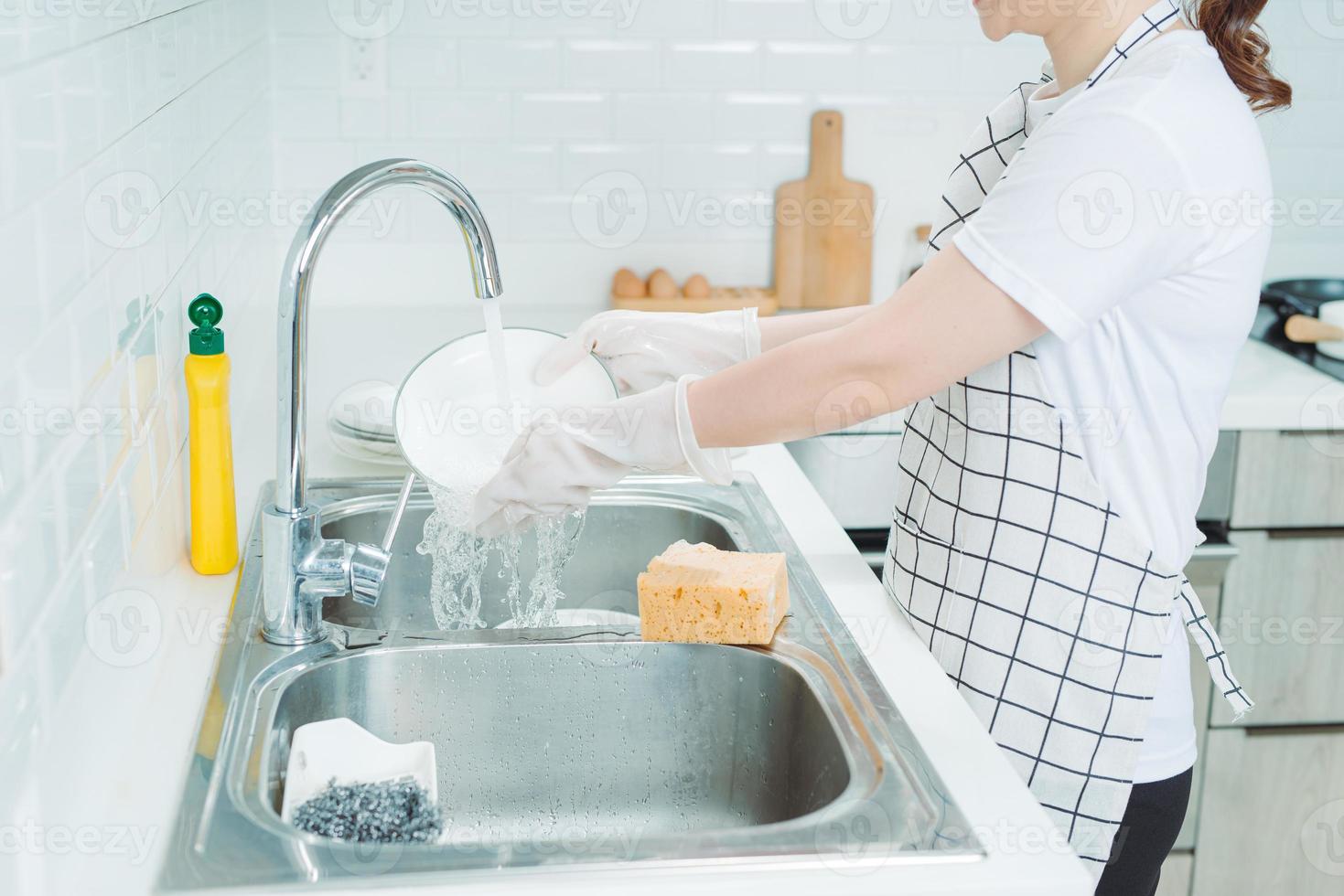 Beautiful smiling young woman washing the dishes in modern white kitchen. photo