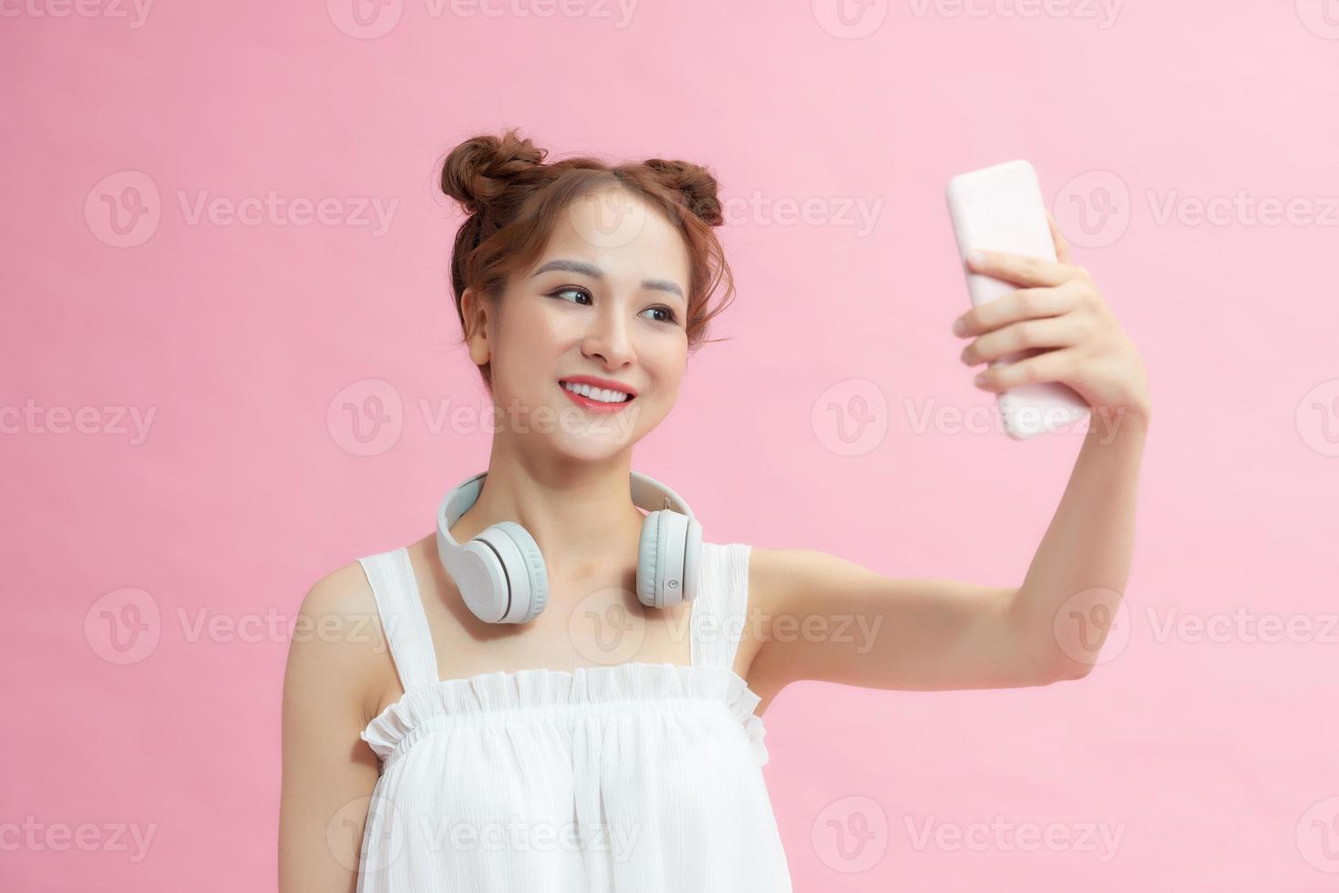 Portrait of charming young woman smiling while taking selfie photo isolated over pink background