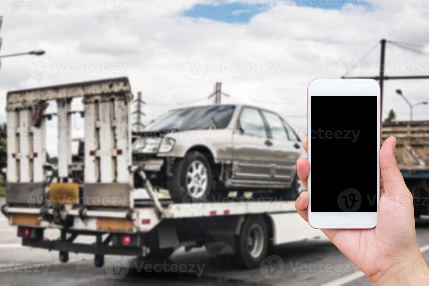 Hand using mobile smartphone for emergency roadside service with Broken car on tow truck after traffic accident background photo