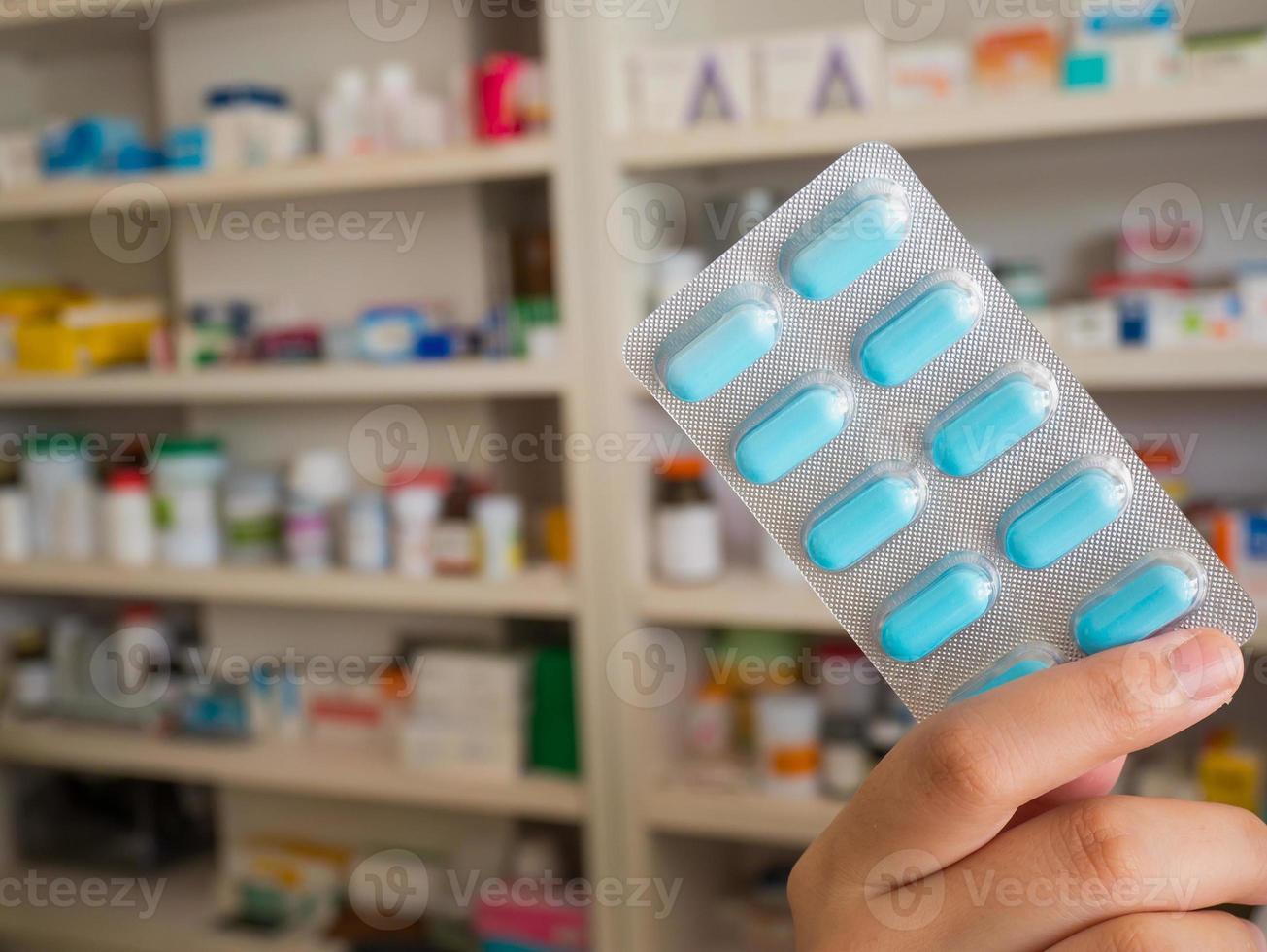 Farmacéutico que muestra píldoras de medicina con fondo de estantes de farmacia foto