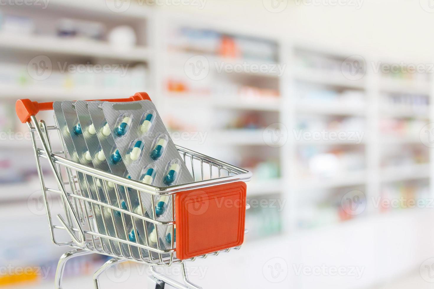 Medical pills capsule in shopping cart with pharmacy drugstore shelves blurred background photo