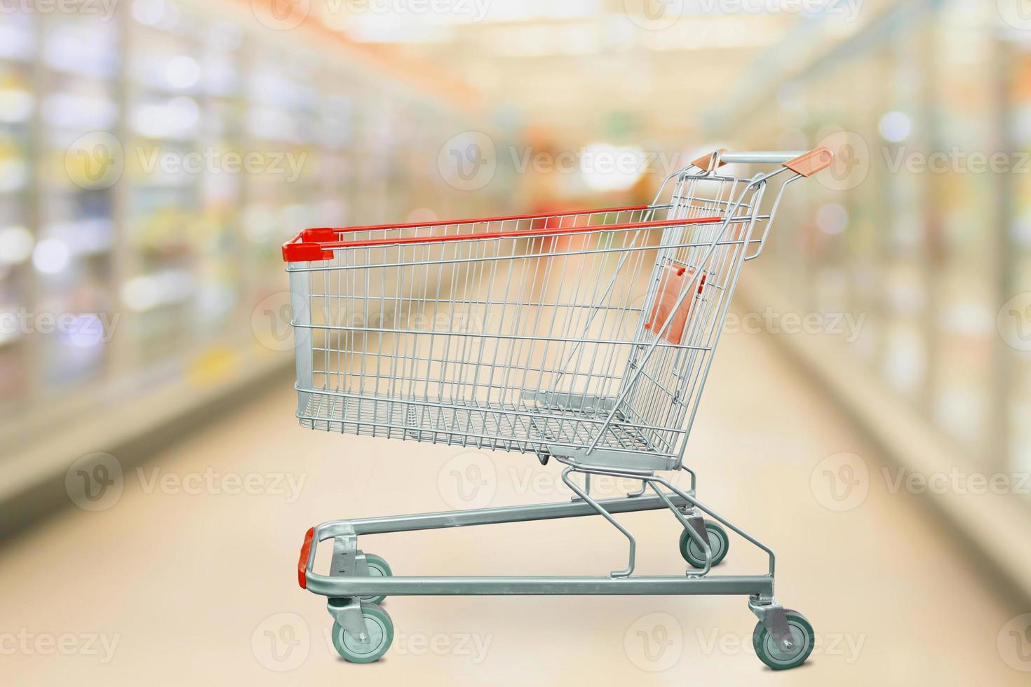 Supermarket refrigerators freezer aisle blur defocused background with empty red shopping cart photo