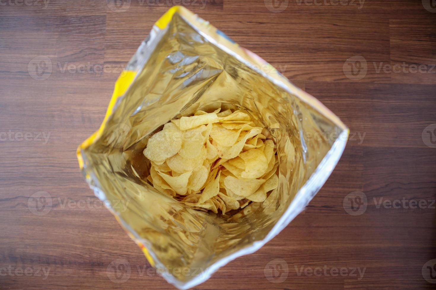 Potato chips in open snack bag close up on table floor photo