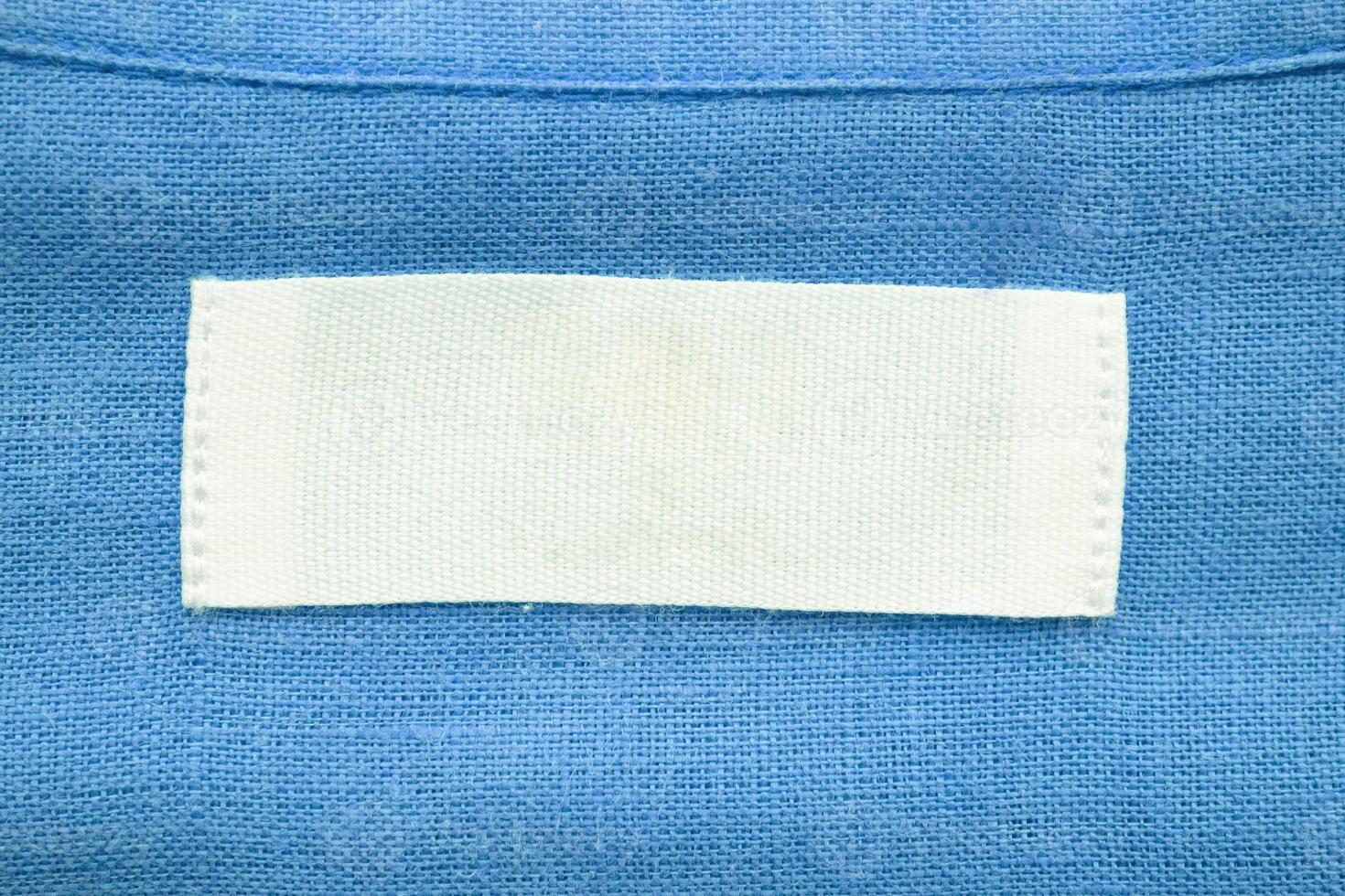 White blank clothing tag label on blue linen shirt fabric texture background photo