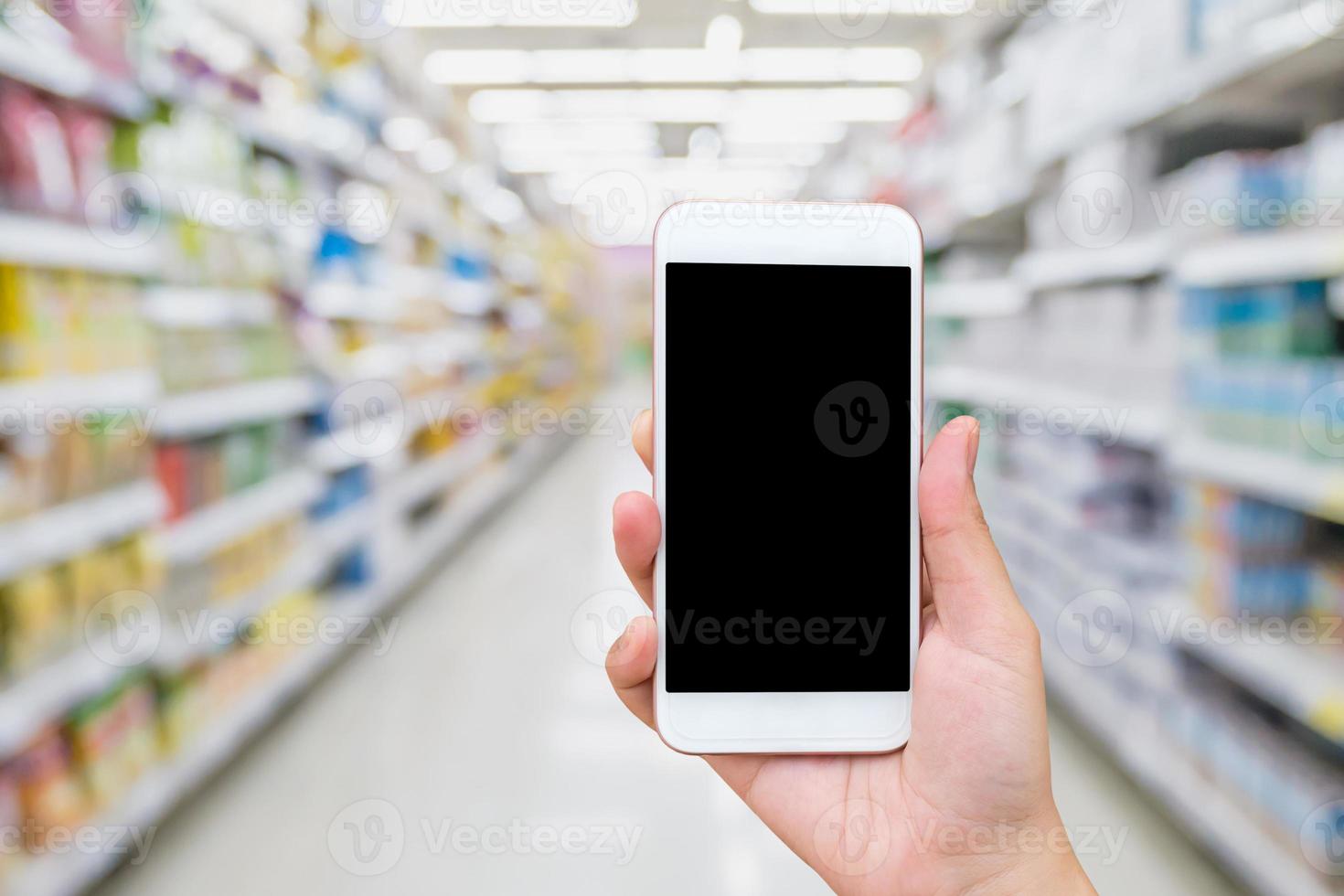 Female hand holding mobile phone with supermarket background photo